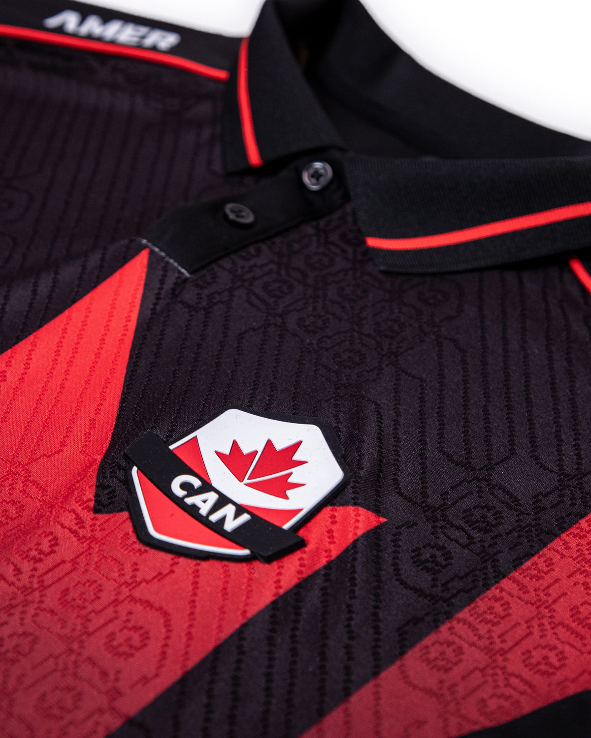 Close-up of a black and red patterned polo shirt with a black collar trimmed in red, featuring a Canada shield patch on the chest.